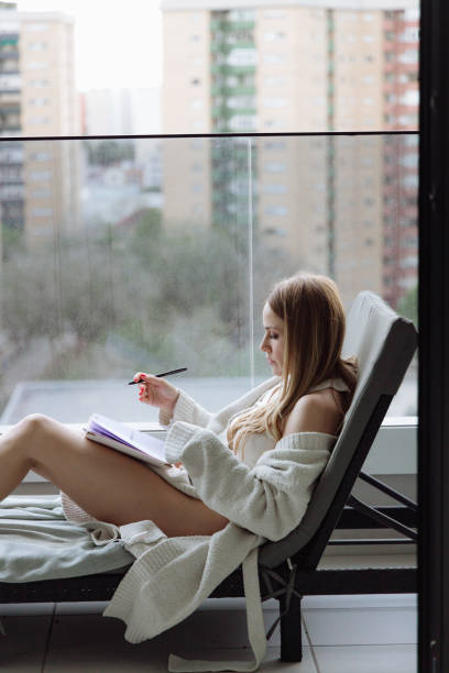 istock Young woman reading a book lying down on sofa 2161720023