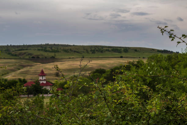 A peaceful scene depicting a solitary cabin nestled atop a lush green hill, illuminated by the warm hues of sunset. The surroundings provide a serene atmosphere, complemented by the calm sea horizon.