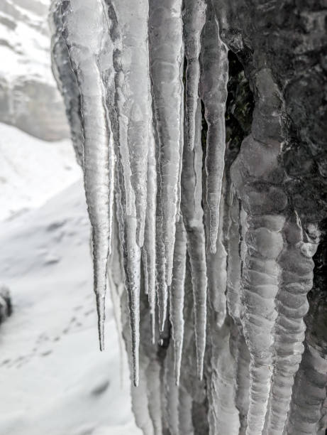 Close-up of long icicles hanging from the rocky overhang near Kvernufoss waterfall in Iceland during winter, with snowy and icy formations creating a stunning natural scene.