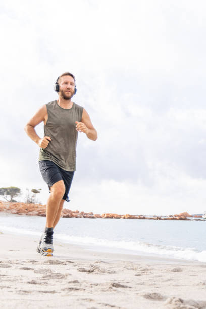 istock Man Jogging on Beach with Headphones 2161742312