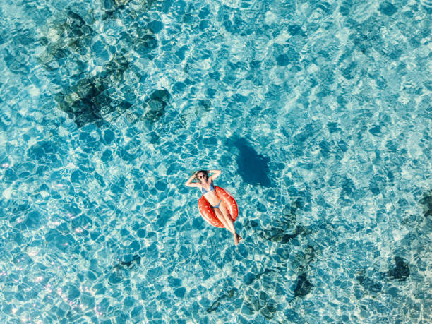 istock Woman Relaxing with Hands Behind Head on Float in Clear Waters 2161745035
