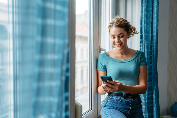 istock Young Woman Using Phone By The Window In The Morning 2161748405