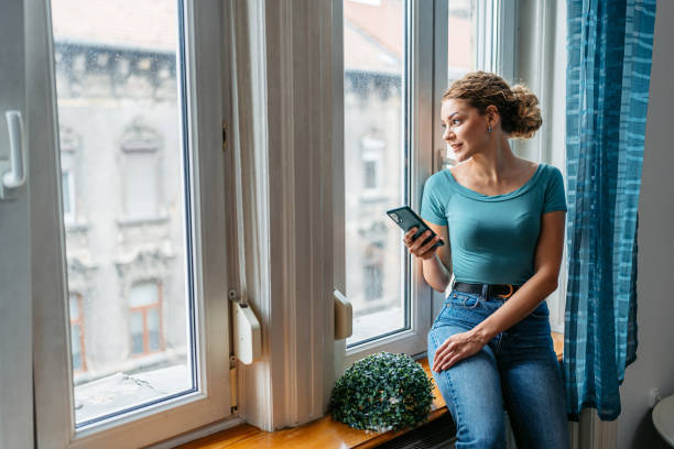 istock Young Woman Using Phone By The Window In The Morning 2161748583