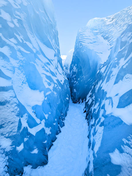 A mesmerizing view of a narrow ice crevasse on Skaftafell Glacier in Iceland, with smooth, blue ice walls and a bright sky above, showcasing the stunning beauty and intricate formations of the glacier.