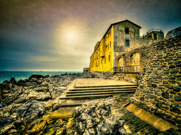 Cefalù, Italy - Stone steps leading up to a yellow building with an archway, overlooking the coastline.