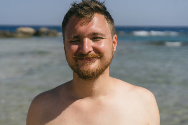 istock A young man with a beard smiles at the camera while standing in the shallow water on a sunny day 2161755475