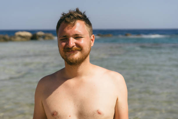 istock A young man with a beard smiles at the camera while standing in the shallow water on a sunny day 2161755480