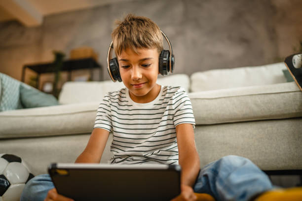 istock young boy with headphones sit on the floor and use digital tablet 2161756217