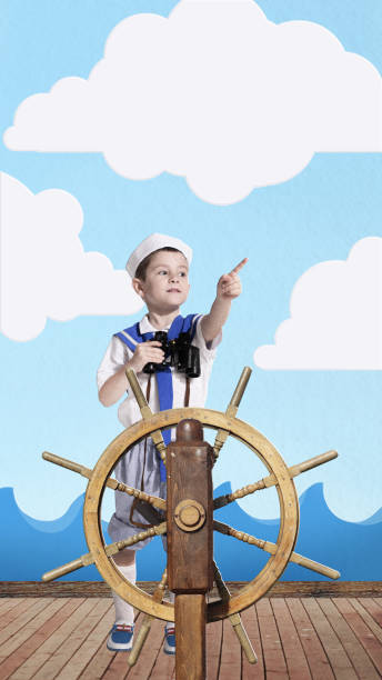 istock Young boy dressed as sailor standing confidently at ship helm, holding binoculars and pointing ahead. Contemporary art collage. 2161764433