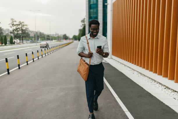 istock Man walking down a street while looking at his phone. 2161765392