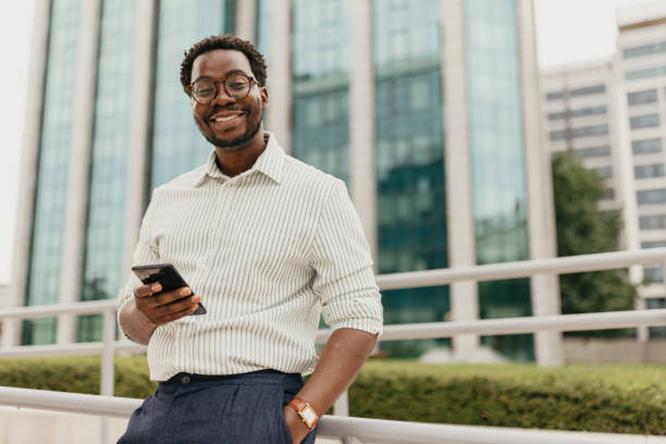 istock Smiling man in striped shirt using phone outdoors. 2161765990