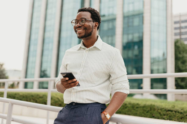 istock Man in striped shirt using phone next to tall building 2161766028