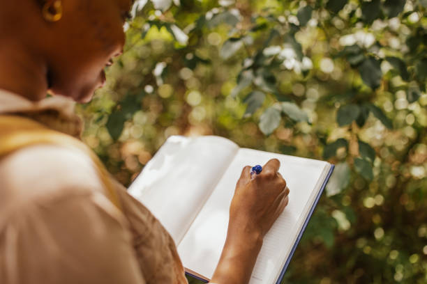 istock Close-up of woman writing in notebook under trees 2161766039