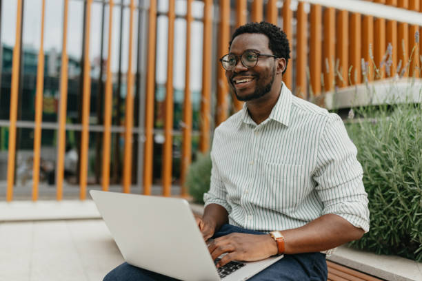 Man smiling while working on laptop in outdoor setting