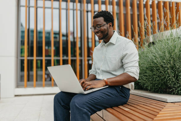 istock Man using laptop on wooden bench in urban setting outdoors. 2161766436