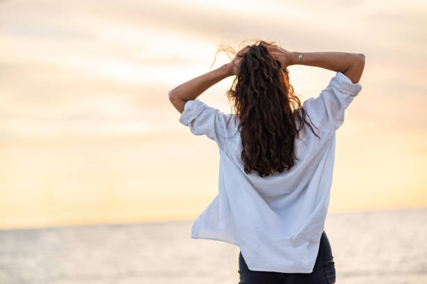 Rear view of woman whit brown curly hair looking at beautiful sunset on the beach