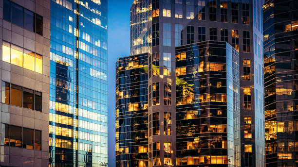 Modern glass offices at dusk Office lights illuminating a collection of modern downtown office towers after sunset. generic description stock pictures, royalty-free photos & images