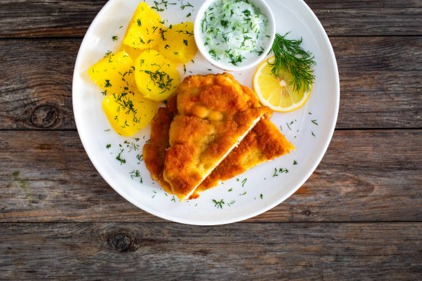 istock Crispy breaded seared chicken cutlet with boiled potatoes and cucumbers in cream served on white plate on wooden table 2161784491