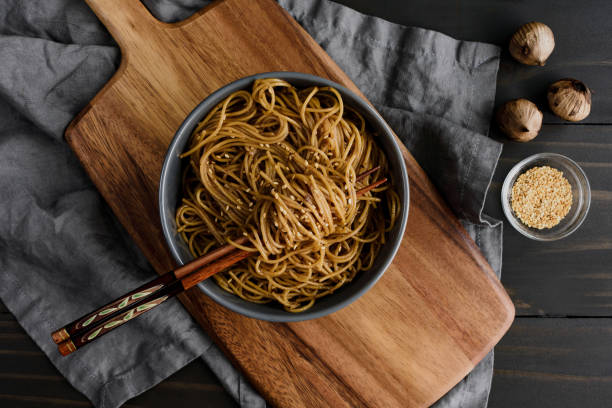 Black Garlic Sesame Noodles Served in a Bowl with Chopsticks Overhead view of chopsticks wrapped in pasta and roasted garlic-sesame sauce in a bowl bamboo twist stock pictures, royalty-free photos & images