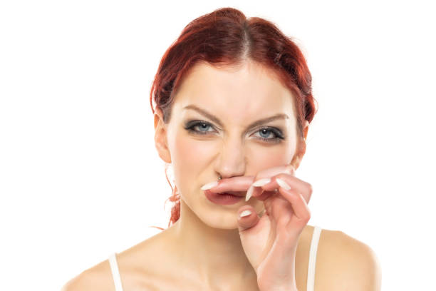 A young redhead woman has itching in the nose on white studio background.
