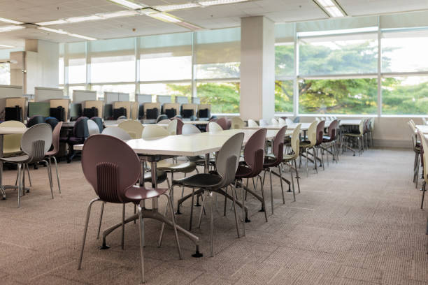 Interior view of a modern Bangkok university library. Rows of empty workstations, each equipped with an office chair and a desktop computer, stretch across the area.