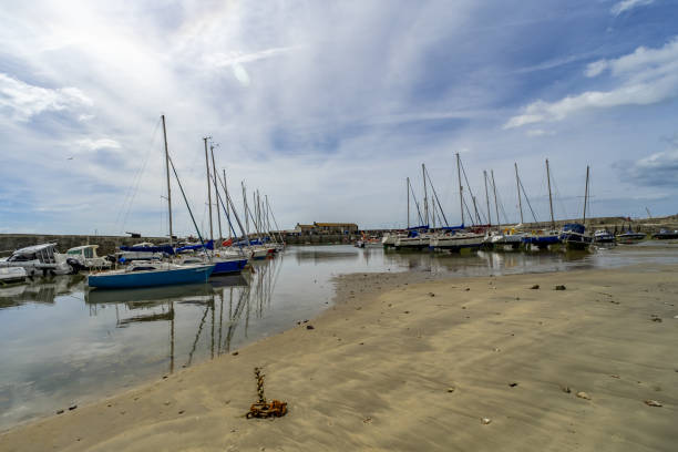 Lyme Regis, Dorset, UK – July 02 2024. Low tide in Lyme Regis Harbour on the Jurassic coast. Boats beached on the sand.