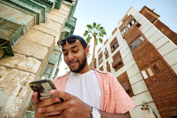 Smiling Saudi man using smart phone in Al-Balad district Low angle view of smiling Saudi man using smart phone while standing in front of building arabian sunglasses stock pictures, royalty-free photos & images