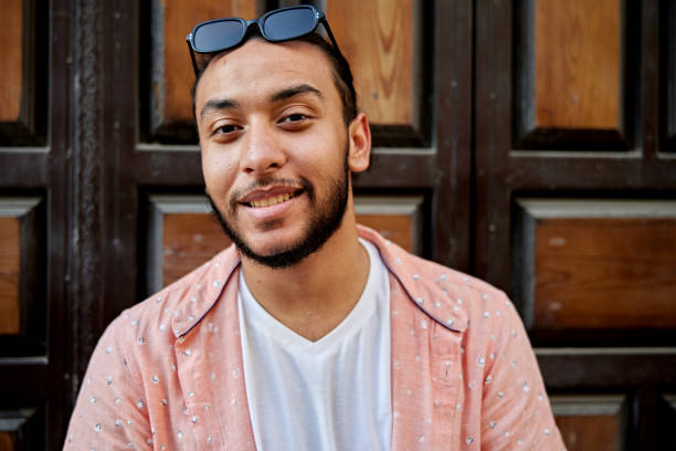 Portrait of smiling young Saudi man with sunglasses against door