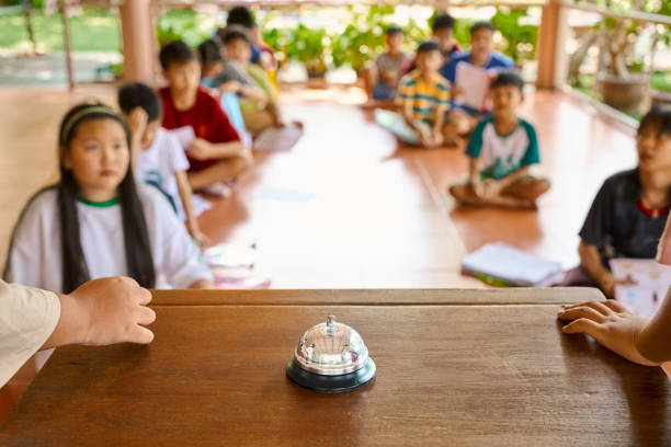Call bell on desk with students sitting on floor during a game at outdoor class