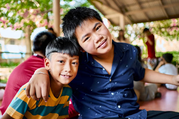 Older brother hugs younger brother ,by the neck, shoulders with big smile on green mountain background in a countryside Laos.