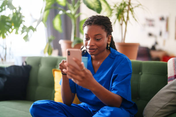 istock Woman in scrubs using mobile phone at home. 2161808032