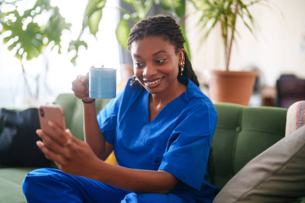 istock Woman in scrubs using mobile phone at home. 2161808033