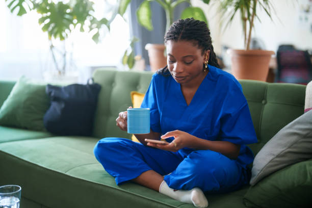 istock Woman in scrubs using mobile phone at home. 2161808092