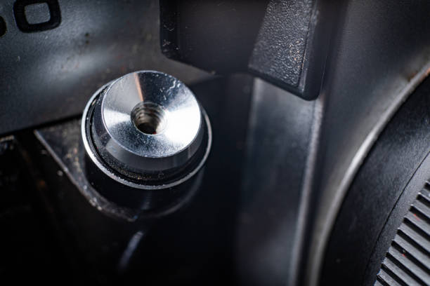 A close-up shot of the shutter button on a vintage photography camera. The metal button is shiny and slightly worn, reflecting the light around it. The camera's black body is partially visible in the background.