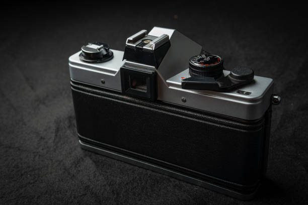 A close-up of a vintage silver photography camera, featuring a black leather bottom and several silver and black controls on the top, resting on a black surface.