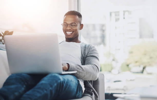 istock Relax, typing and black man with laptop on sofa for remote work, email or communication in living room, Online, illustrator and person for freelance career, browsing internet or proposal in home 2161813708