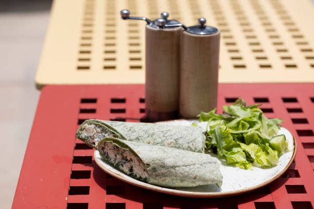 A fresh and healthy spinach wrap filled with creamy chicken salad, cut in half and displayed on a wooden board. The wrap is complemented by salt and pepper shakers in the background