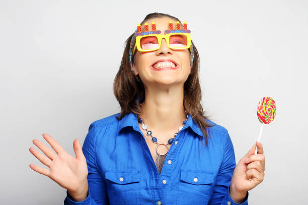 Young woman playfully holds up oversized black glasses, her expression amusingly stern in a light-hearted setting