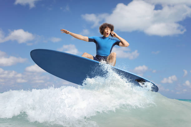 Guy in a wetsuit on a surfboard using a mobile phone