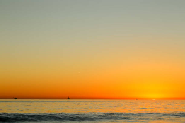 Sunset beach with a surfer on the board, and a cargo boat at the horizon