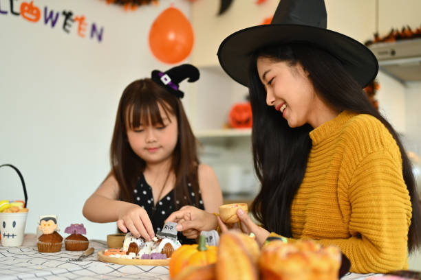 istock Joyful young mother and cute daughter decorating Halloween cupcakes at kitchen table 2161835561