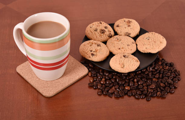 Cookies, coffee beans and mug of coffee with milk on the brown wooden table. Selective focus.