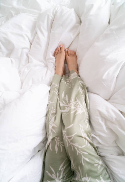 Woman's feet in pajamas on white bed sheets. Relaxation and comfort concept.