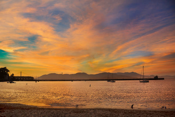 A sunset over San Francisco Bay and the Marin Mountains The sun setting over San Francisco Bay, looking west towards the Golden Gate Bridge with the Marin Hills behind, seen from Fisherman’s Wharf. The harbor front was named after Italian immigrants who moved there after the gold rush; though the wharves have been redeveloped as a tourist attraction from the 1970s the harbor remains an active fishing port. west marin stock pictures, royalty-free photos & images