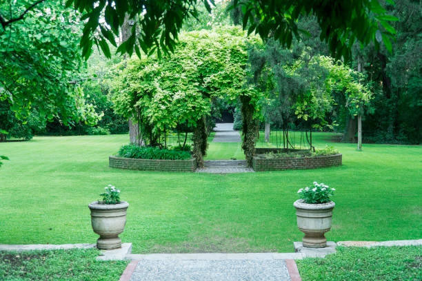 The area in the park is surrounded by green plants and has many white benches. In the middle there is a circle of stones.