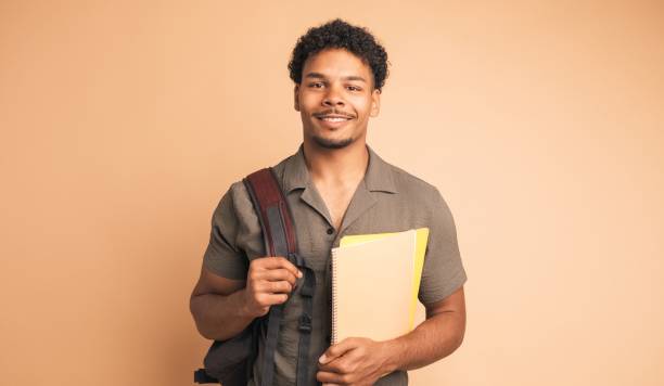 Happy male university student with backpack and books in beige studio