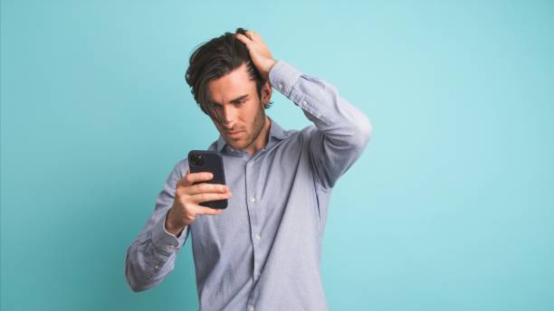 istock Man feeling upset about losing lottery on smartphone in blue studio 2161862920