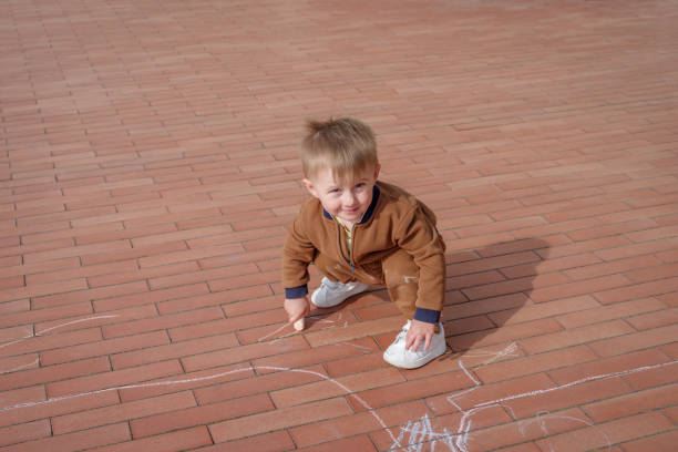 Little boy doodling with chalk on pavement, overhead view