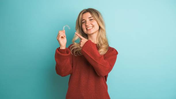 Happy young woman showing invisible braces in blue studio
