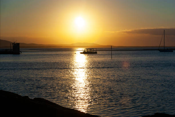 Scenic view of a sunset in Agnes Water, Australia. The sky is painted with vibrant hues of orange, pink, and purple as the sun sets over the horizon, creating a picturesque and tranquil atmosphere.